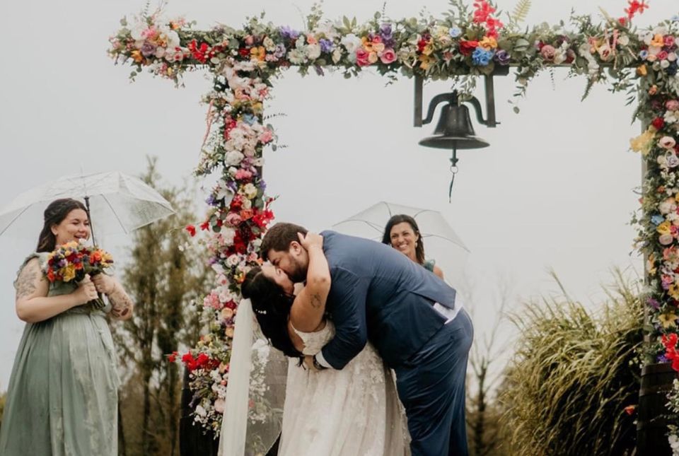 Bride and groom kissing under the arch and bell at The Farmhouse at Emmit Ridge Farm